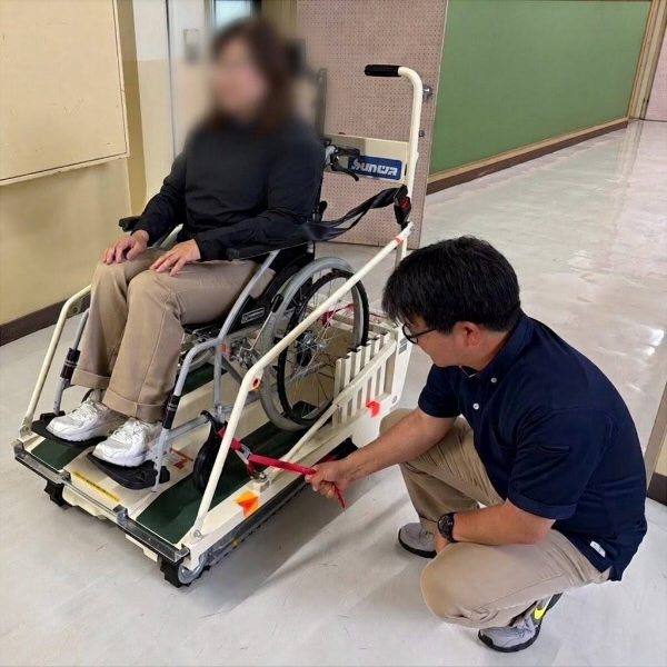 階段昇降車に体と車いすをベルトで固定している様子